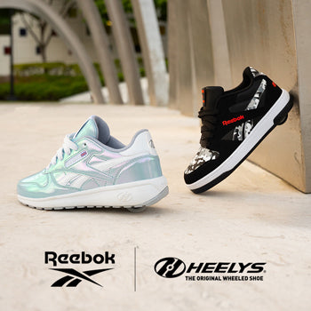 Two pairs of Reebok x Heelys roller shoes, one light blue and one black with red accents, on a concrete surface.