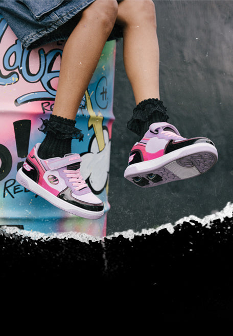 2 Wheel Heelys Shoes. Pink and black dual wheel Heelys roller shoes worn by a child sitting on a colorfully painted barrel.